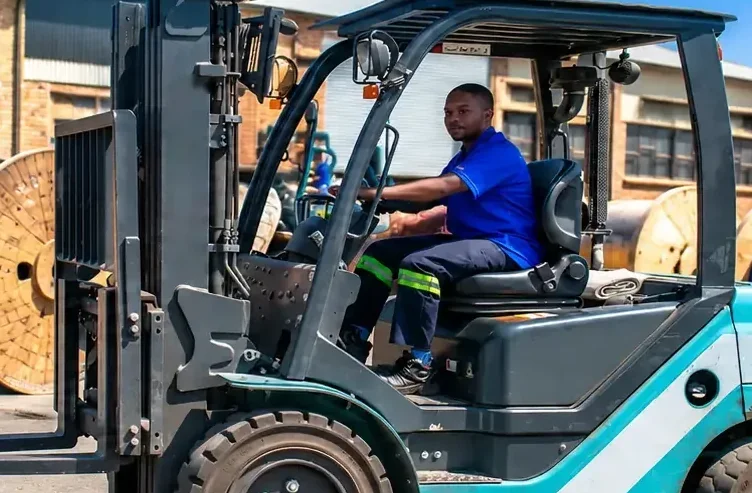 A forklift driver moving wooden cable drums in a cable yard